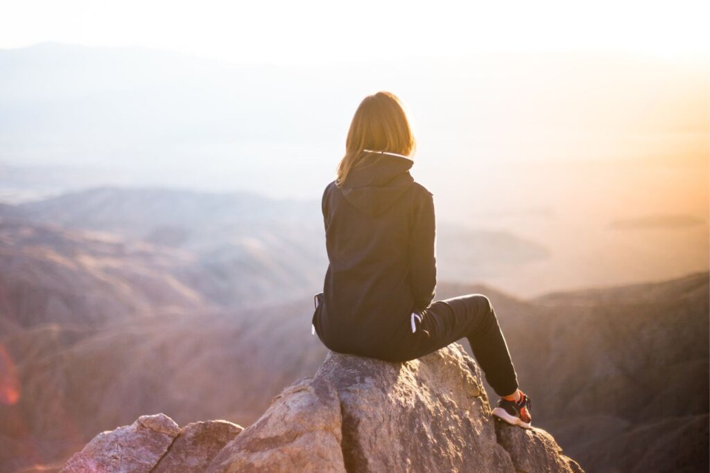Frau sitzt auf Felsen und blickt über die Berge. Wenn ein Elternteil ein zweites Kind will und das andere nicht, kann das die Beziehung extrem belasten.