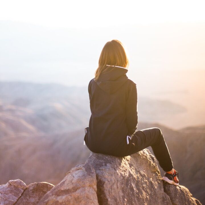 Frau sitzt auf Felsen und blickt über die Berge. Wenn ein Elternteil ein zweites Kind will und das andere nicht, kann das die Beziehung extrem belasten.