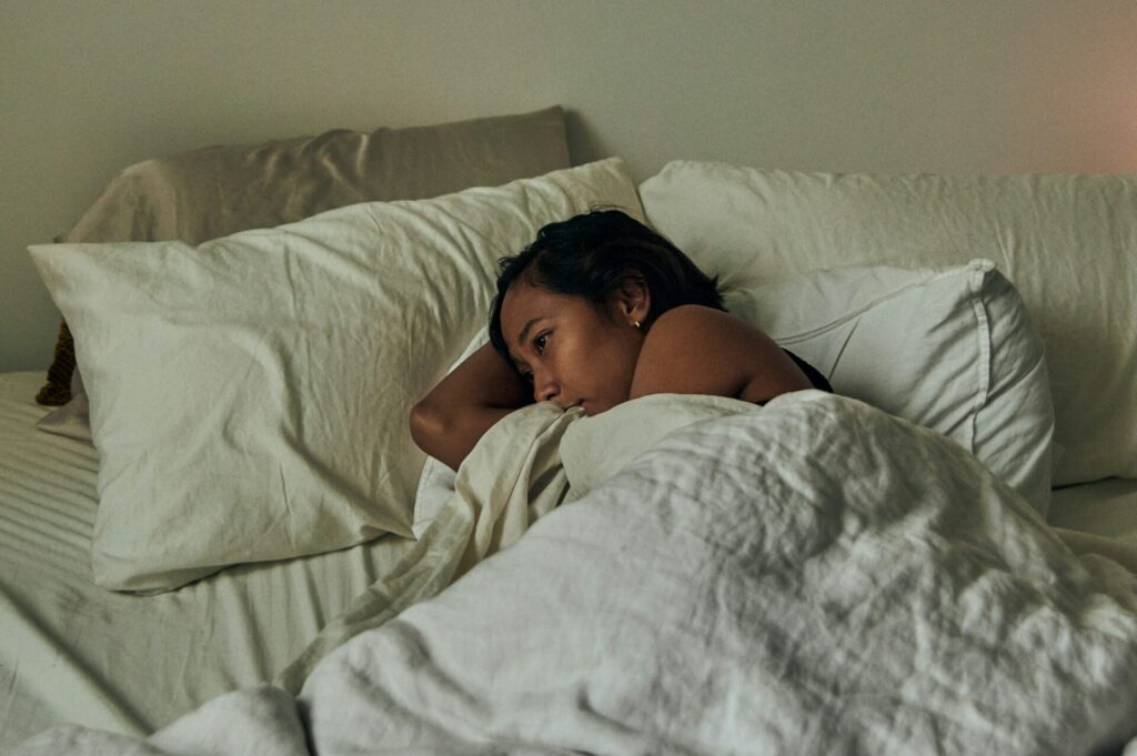 Frau liegt erschöpft im Bett. - Viele Mütter sind überfordert.