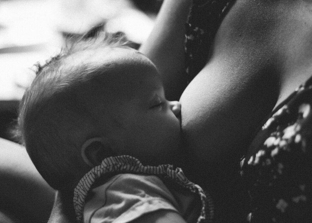 Ein Baby trinkt mit geschlossenen Augen an der Brust seiner Mutter. Wo und mit wem soll ich gebären? Tipps von einer Doula.