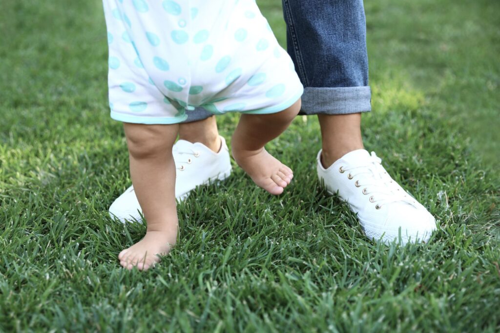 Ein Kleinkind und eine junge Frau laufen durch Gras, man sieht nur ihre Füsse. Erfahrungen und Tipps zur Au-pair-Suche in der Schweiz.