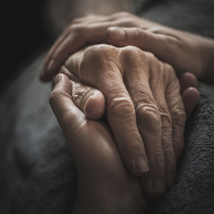 Zwei Hände halten die Hand einer älteren Person. Wenn zur Betreuung der Kinder die Pflege der eigenen Eltern kommt, ist die Belastung gross.