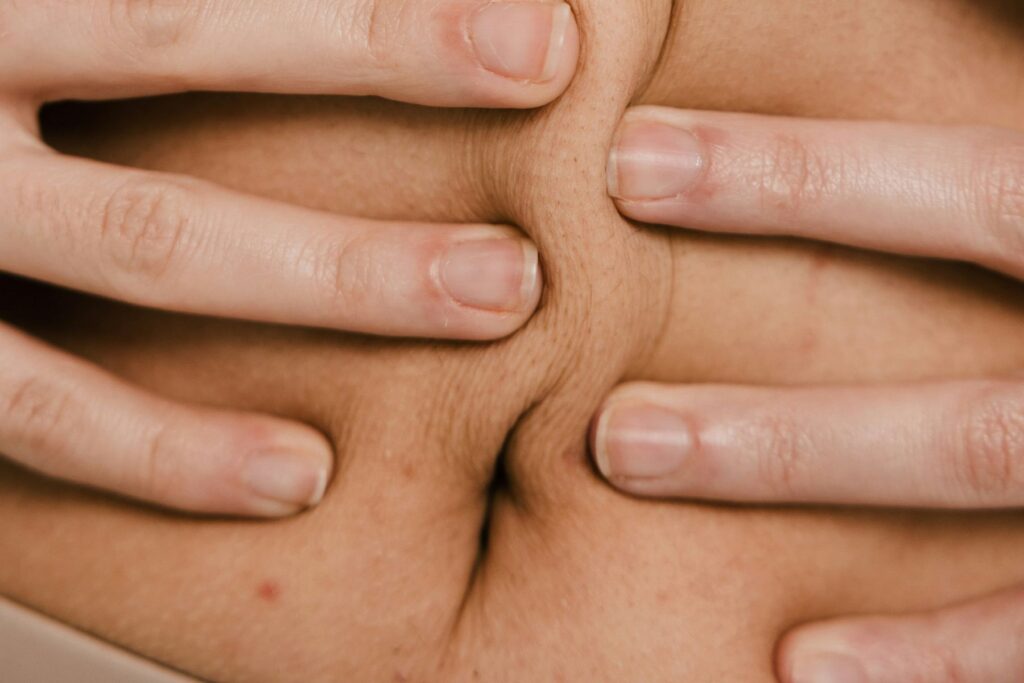 Bauch, der von zwei Händen links und rechts vom Bauchnabel zusammengedrückt wird. Was sagt das Gewicht über die Gesundheit aus? Nicht viel.