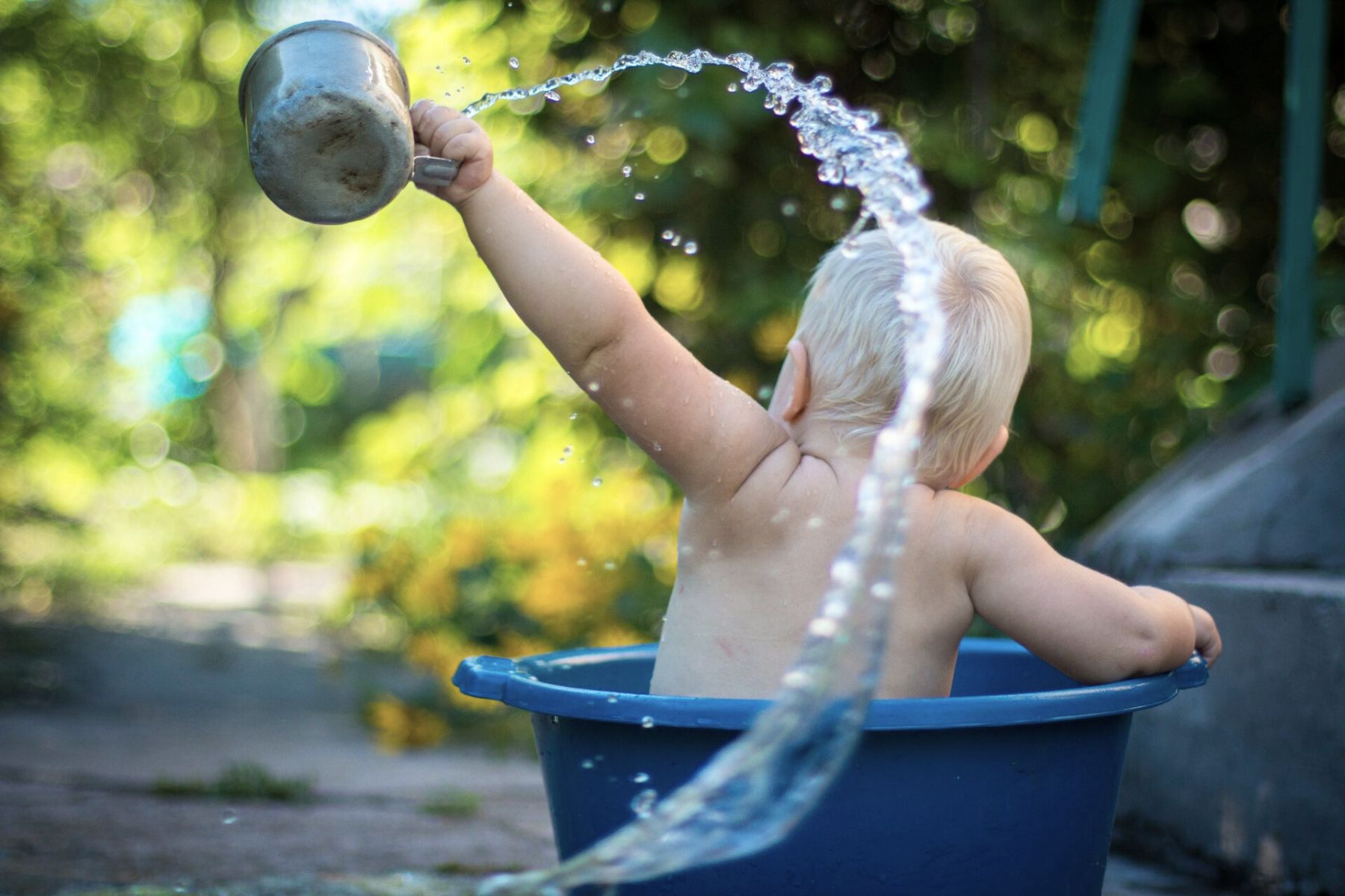 Ein Kleinkind badet in einem Eimer sitzend und giesst in hohem Bogen Wasser in die Luft. Spiel jetzt unser Badi Bullshit Bingo für Eltern!