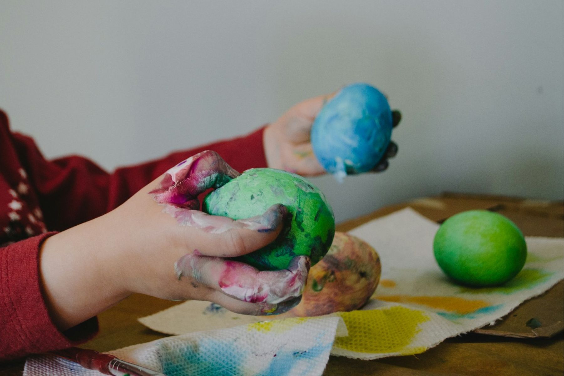 Farbige Kinderhände halten gefärbte Ostereier. - Basteln für Ostern mit kleinen Kindern? Wir haben einfache Ideen, die garantiert gelingen.