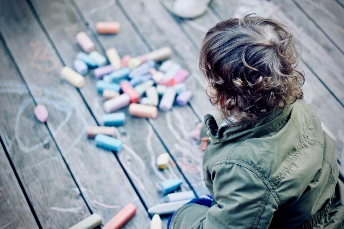 Junge malt mit Kreide auf einen Holzboden im Freien. Viele Eltern spielen nicht gern - doch fällt es ihnen schwer, Nein zu sagen. Hier kommt Entlastung!