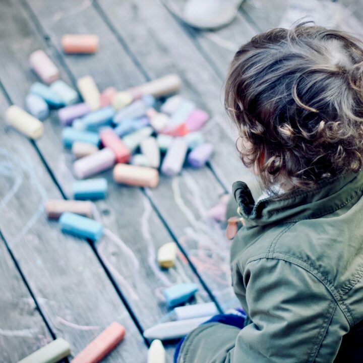 Junge malt mit Kreide auf einen Holzboden im Freien. Viele Eltern spielen nicht gern - doch fällt es ihnen schwer, Nein zu sagen. Hier kommt Entlastung!
