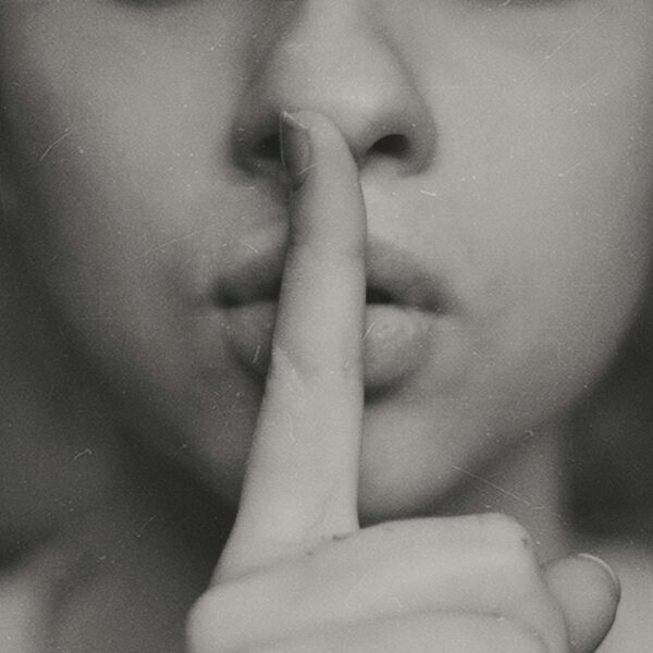 Person hält sich den Finger an die Lippen, als Symbol für leise sein oder Geheimnis.