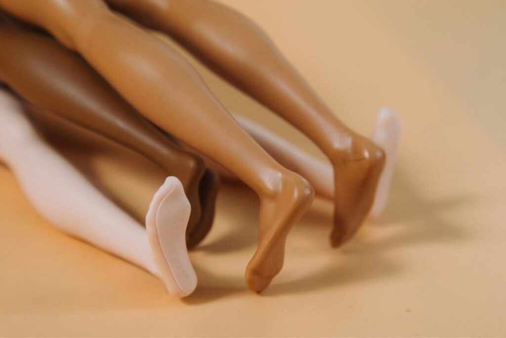Drei Paar Barbie-Beine, eins dunkelhäutig, eins hellhäutig, eins dazwischen, über einander liegend.