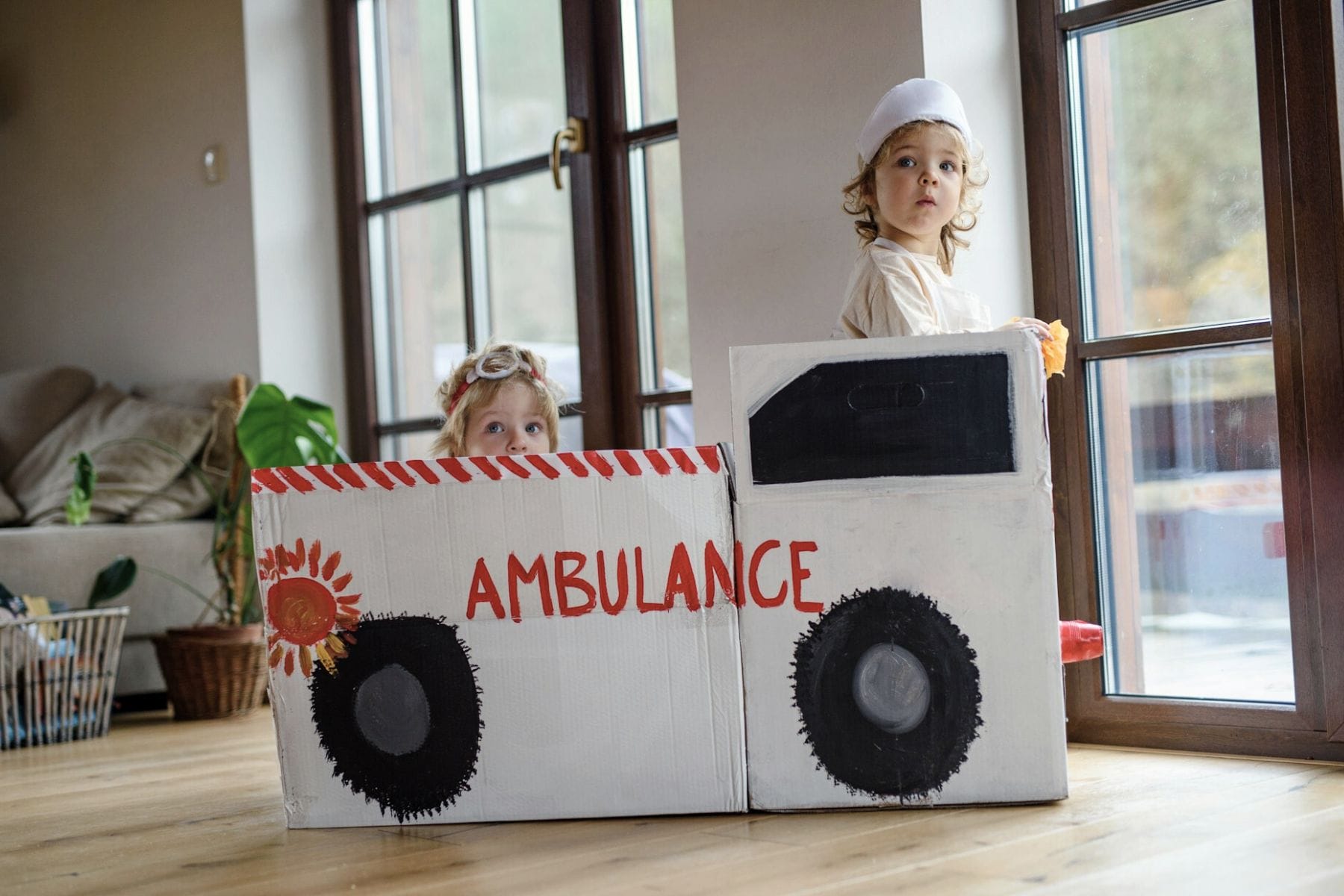Zwei Kinder sitzen in einem aus Kartonkisten gebastelten und mit "Ambluance" beschrifteten Krankenwagen. Krankenkasse – Antworten&Checkliste