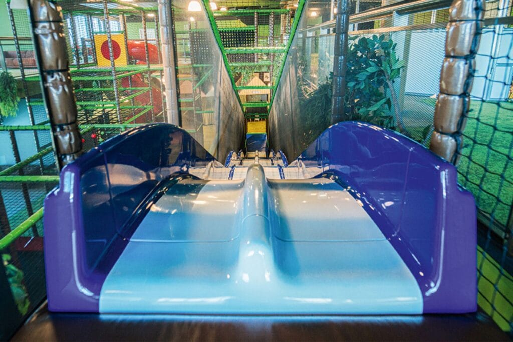 Blaue Wellen-Rutschbahn, von oben betrachtet, im Hintergrund grüne Klettergerüste. Ostschweiz mit Kindern bei Regen, unsere erprobten Tipps.