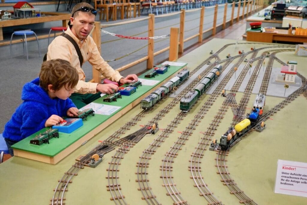 Vater und Sohn bedienen die Schaltknöpfe einer Modelleisenbahn in der Erlebniswelt Toggenburg. – Tipps für Ostschweiz mit Kindern bei Regen