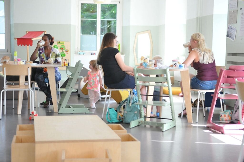 Eltern und Kinder sitzen im Familienzentrum Schaffhausen an Tischen und trinken etwas, überall hat es Spielsachen. - Ostschweiz mit Kindern bei Regen