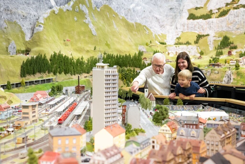 Ein älterer Mann, eine junge Frau und ein kleiner Junge betrachten eine Miniaturwelt bei Smilestones. - Ostschweiz mit Kindern bei Regen