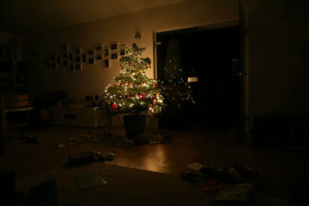Dunkles Wohnzimmer, in der Mitte ein hell leuchtender, geschmückter Weihnachtsbaum. Gibt es überhaupt ein Christkind? Vom Ende der Täuschung