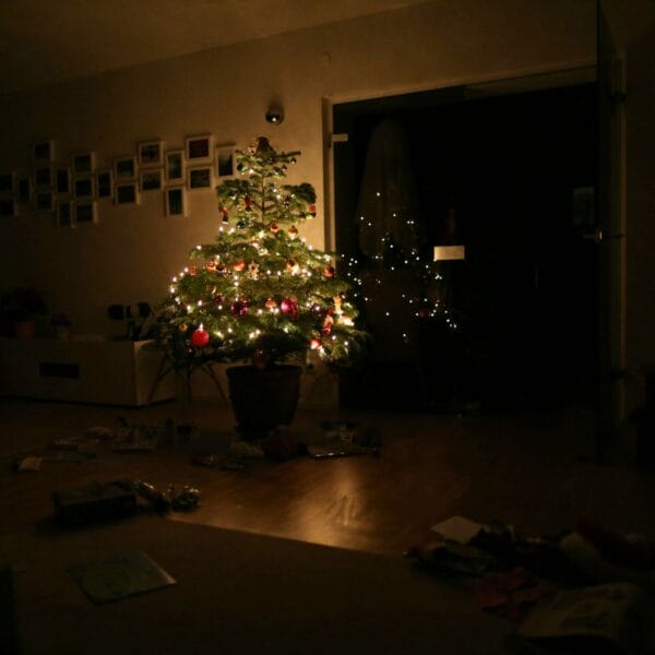 Dunkles Wohnzimmer, in der Mitte ein hell leuchtender, geschmückter Weihnachtsbaum. Gibt es überhaupt ein Christkind? Vom Ende der Täuschung