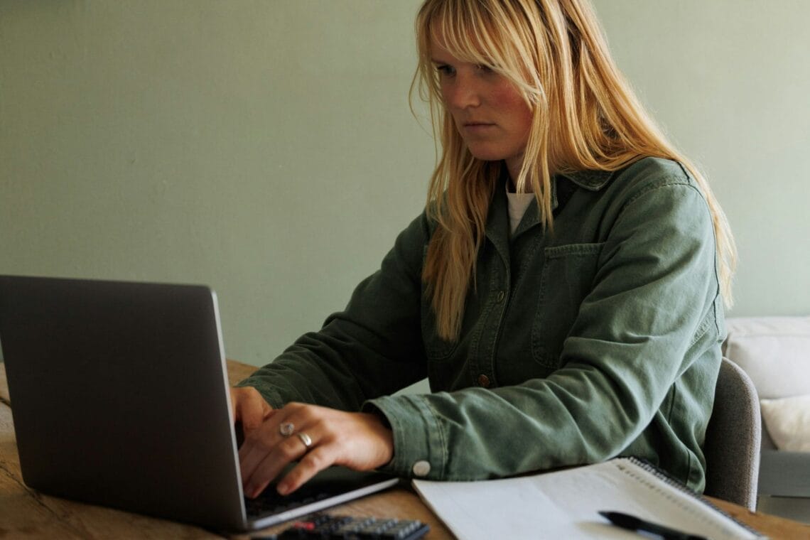 Eine Frau sitzt mit einem Taschenrechner vor ihrem Computer und tippt.