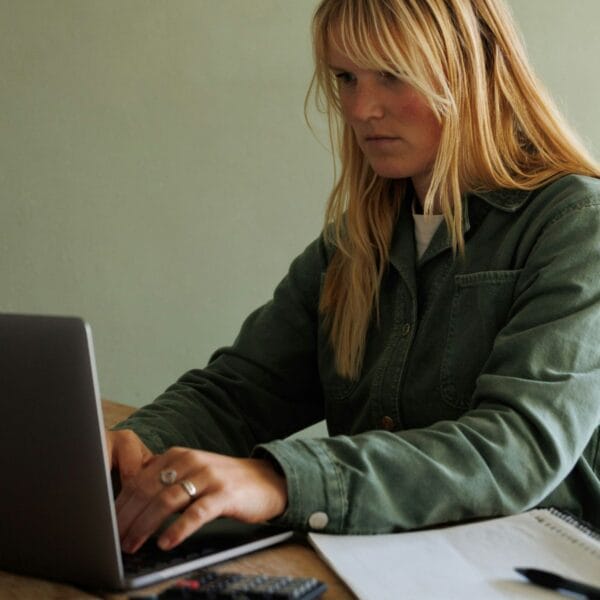 Eine Frau sitzt mit einem Taschenrechner vor ihrem Computer und tippt.