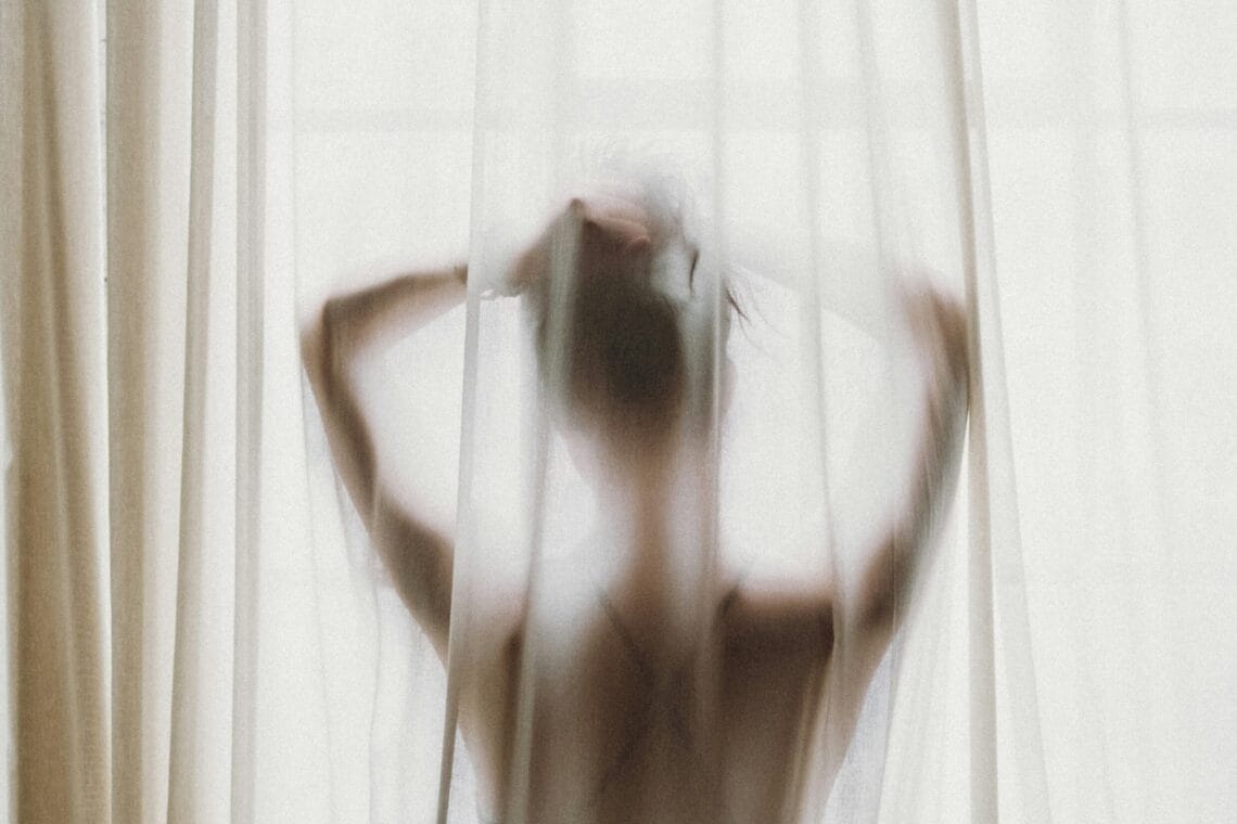 Shilouette einer Frau von hinten, die hinter einem Vorhang steht und sich in die Haare fasst. - Erfahrungsbericht Fremdverlieben
