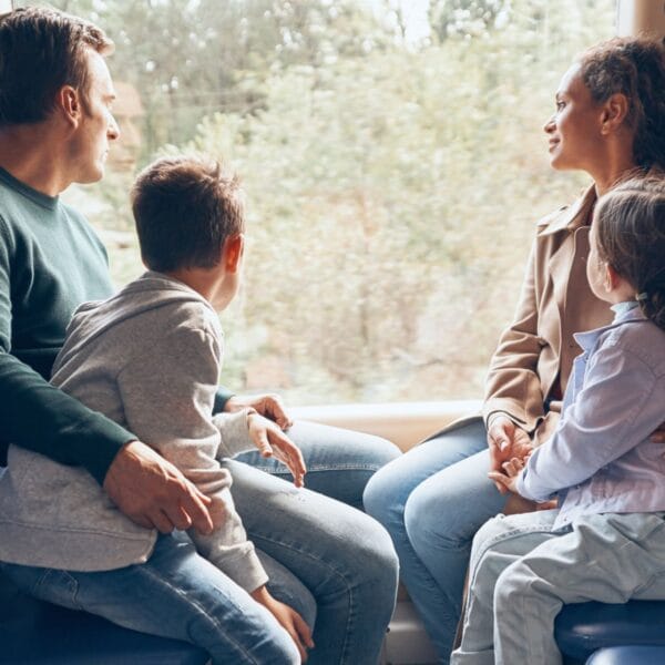 Familie mit Mutter, Vater, Tochter, Sohn sitzt im Zugabteil und schaut aus dem Fenster. Familienferien mit dem Zug? Eine Expertin gibt Tipps