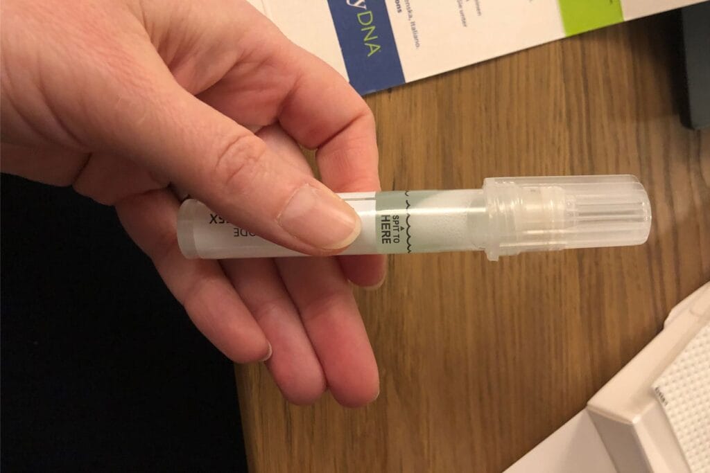 Eine Hand hält einen DNA-Test, ein durchsichtiges Röhrchen mit Schraubdeckel und Markierung "Spit to here". - Erfahrungsbericht Spenderkind