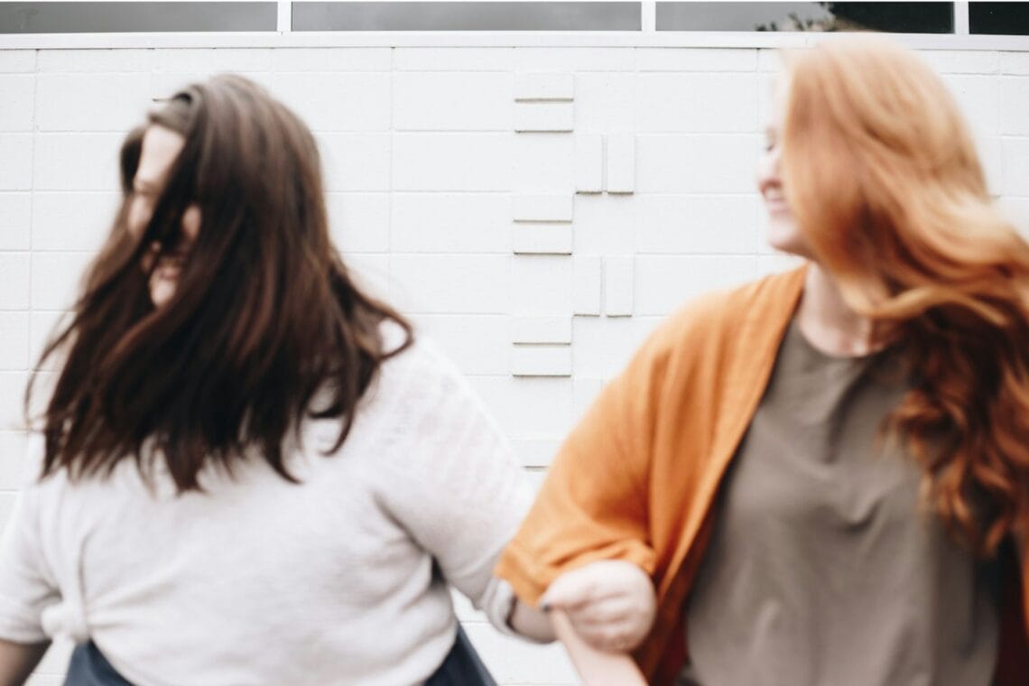 Unscharfe Fotografie von zwei Frauen, die ihre Arme eingehakt haben, eine braun-, die andere rothaarig. – Freundschaft, unterschätzt.