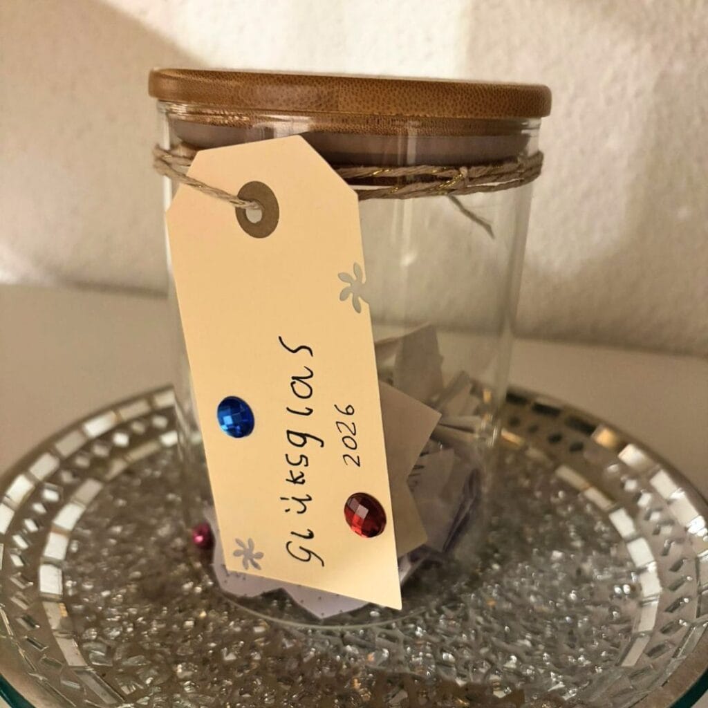 Glas mit Schild dran, auf dem steht: Glücksglas 2026. Schöne Erlebnisse auf Zettel schreiben, von Zeit zu Zeit einen ziehen und vorlesen. - Ein-Eltern-Familie