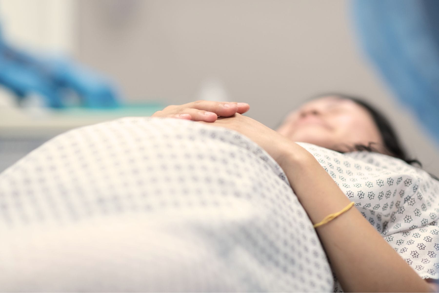 Liegende Frau in Spitalhemd von unten fotografiert, der Fokus liegt auf ihrem schwangeren Bauch. - Einleitung der Geburt, Erfahrungsbericht