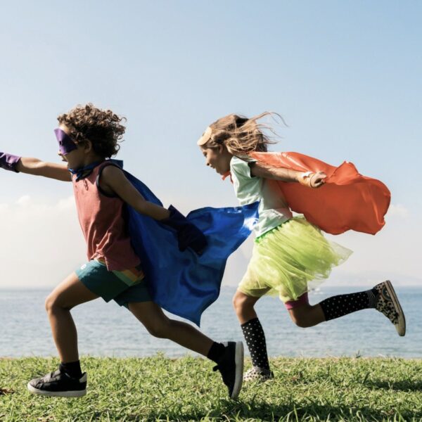 Junge und Mädchen rennen mit Superhelden-Umhang über eine Wiese. - Typisch Mädchen, typisch Jungs? Genderdiskussionen mit einem Erstklässler