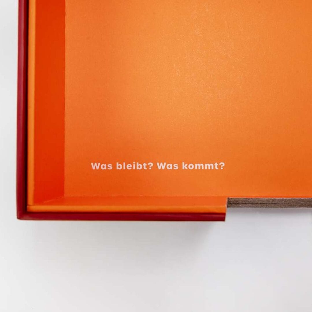 Orange Innenseite der Box mit Aufdruck «Was bleibt? Was kommt?»